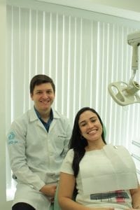 Dentista Vinícius, sentado ao lado de uma paciente em sua clínica odontológica